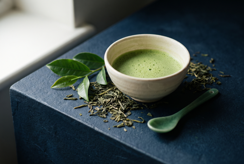 Loose green tea leaves and a ceramic bowl of matcha on dark stone, the green tea note in perfume