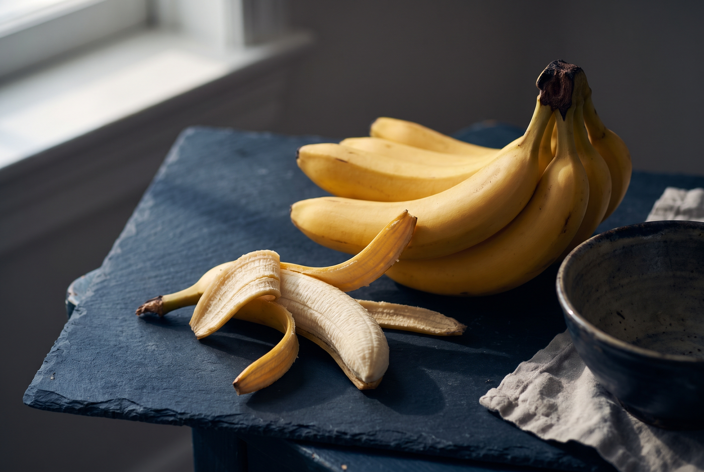 Ripe bananas with one partly peeled on dark slate, the banana note in fragrance