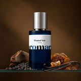 Aromara Wanted Noir Extrait perfume bottle with black peppercorns, vanilla pod, amber resin, and sandalwood on a clear glass shelf, deep amber backdrop
