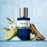 Aromara Pacific Breeze Extrait perfume bottle with sea salt crystals, halved bergamot, white tea flowers, and cedar wood on a clear glass shelf, pale ice-blue aquatic backdrop