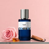 Aromara Baddie Blush Extrait perfume bottle on glass shelf with pink rose, amber resin, vanilla pod and sandalwood on soft blush pink background