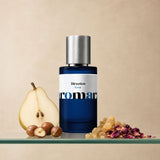 Aromara Direction Extrait perfume bottle on glass shelf with pear, hazelnuts, frankincense resin, and dried rose petals on warm beige background