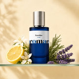 Aromara Portofino Extrait perfume bottle with halved lemon, white neroli flowers, lavender sprig, and rosemary on a clear glass shelf, pale yellow Mediterranean backdrop