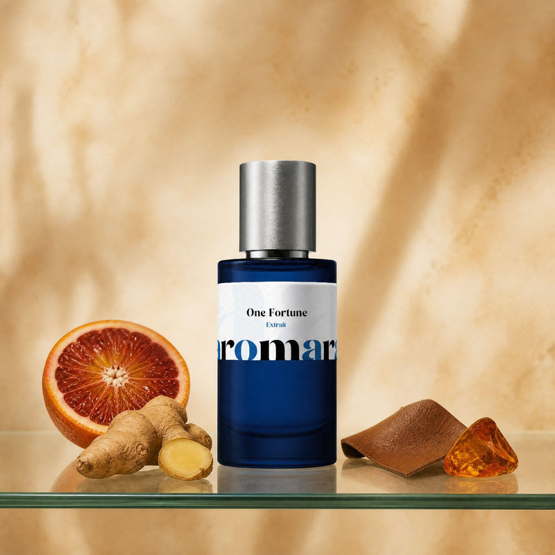 Aromara One Fortune Extrait perfume bottle on glass shelf with blood mandarin, fresh ginger root, tan leather and raw amber stone on warm amber background
