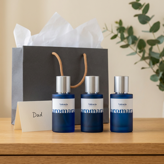 Three blue perfume bottles with silver caps on a wooden surface, next to a gift bag and card.