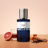 Perdu by Aromara on a pale apricot blush to burnt-orange caramel background with a halved blood orange, a glass of rum, caramels, cinnamon sticks and vanilla pods. 35% Extrait, inspired by Roja Parfums Lost in Paris.