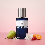 Aria by Aromara on a pale magnolia blush to soft redcurrant pink background with a green pear, lily of the valley, a white magnolia, redcurrants and a halved mandarin. 35% Extrait, inspired by Loewe Aire Sutileza.